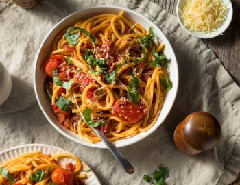 A plate of Bucatini pasta sitting alongside a plate of cheese and a pepper shaker on a table