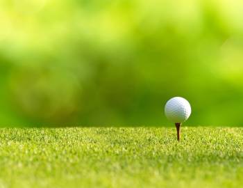 Closeup of a golf ball sitting on a tee with a blurred green background