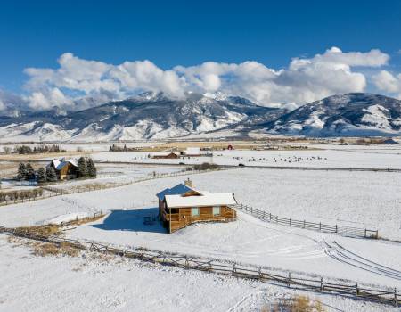 Small cabin in the middle of snowy fields in Montana with mountains in the distance.