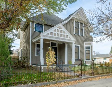 White and grey house behind a black steel fence with a road lined with fallen leaves in front.