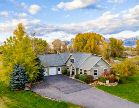 Grey house surrounded by trees during autumn, with a driveway leading up to it.