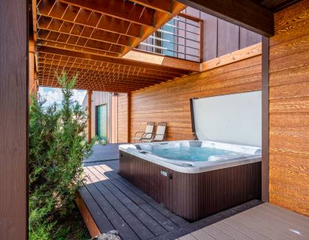 Patio of a brown cabin covered by a roof with a hot tub on the side.