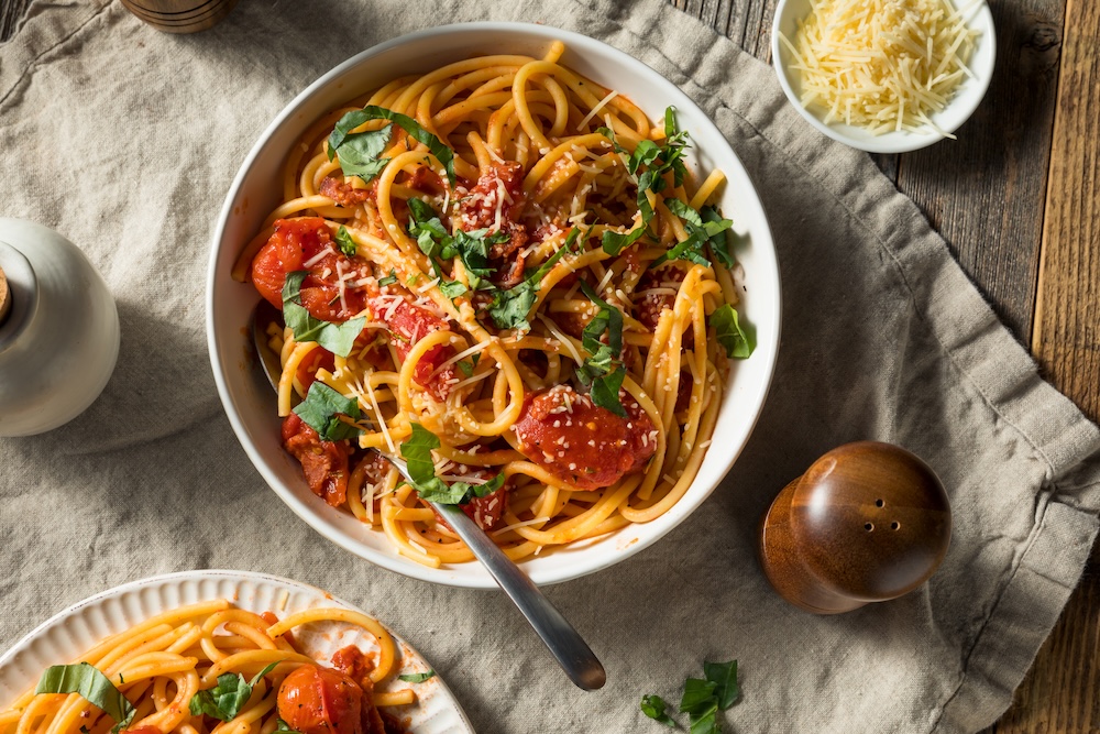 A plate of Bucatini pasta sitting alongside a plate of cheese and a pepper shaker on a table