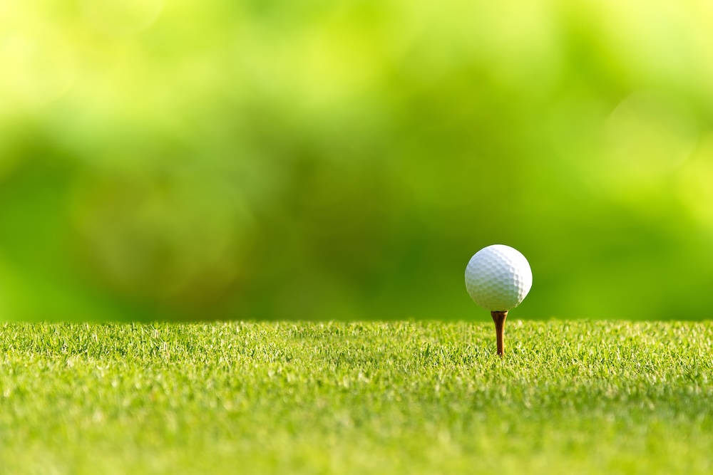 Closeup of a golf ball sitting on a tee with a blurred green background